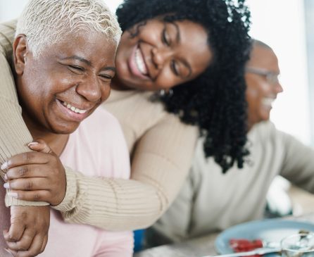 African daughter hugging her mum during lunch meal at home - Love and family concept - Main focus on senior woman face